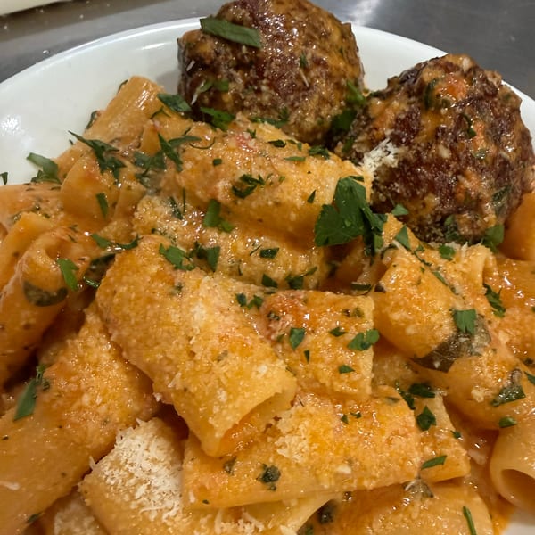 Rigatoni pasta with creamy tomato sauce, grated cheese, fresh herbs, and two large meatballs.