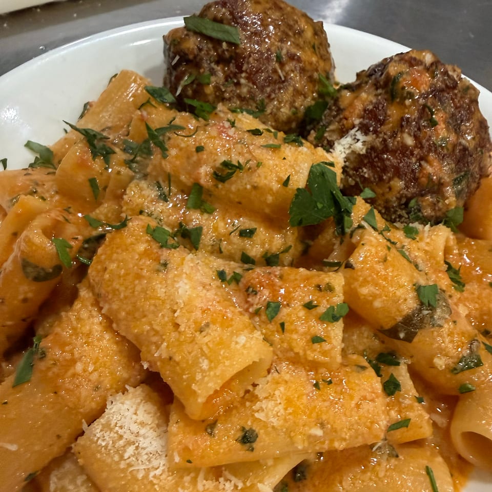 Rigatoni pasta with creamy tomato sauce, grated cheese, fresh herbs, and two large meatballs.
