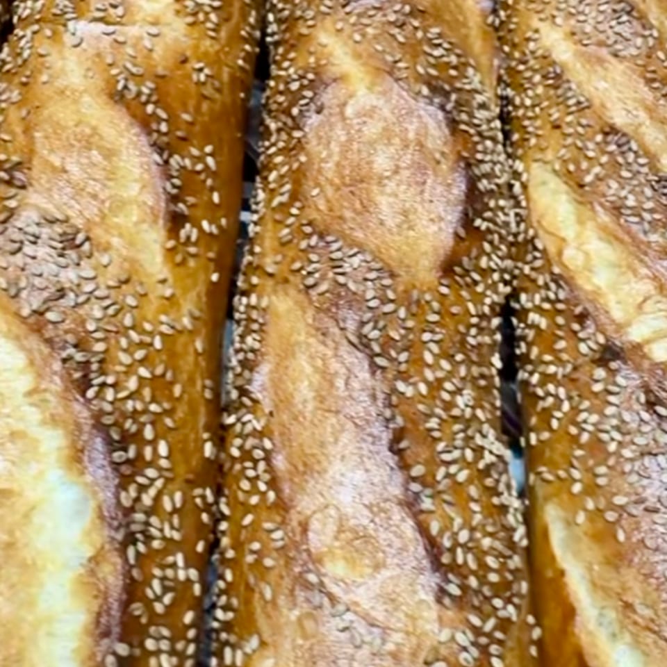 Close-up of golden-brown baguettes, generously sprinkled with sesame seeds, fresh from the oven.